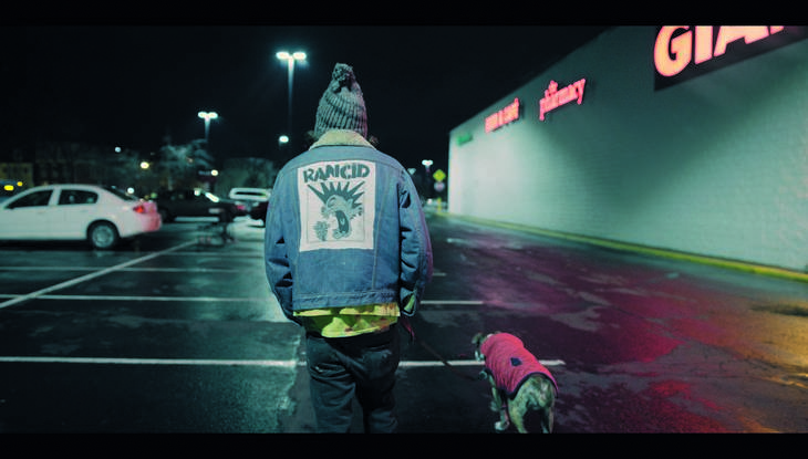 Von hinten: Ein Mann in Jeansjacke geht nachts mit seinem Hund spazieren