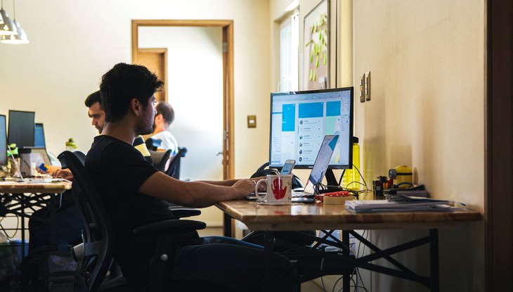 Ein junger Mann sitzt an einem Schreibtisch und schaut auf seinen Computermonitor