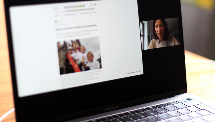 Bildschirmansicht einer Präsentation und rechts daneben Speakerin Ellen Heinrichs auf einem aufgeklappten Laptop