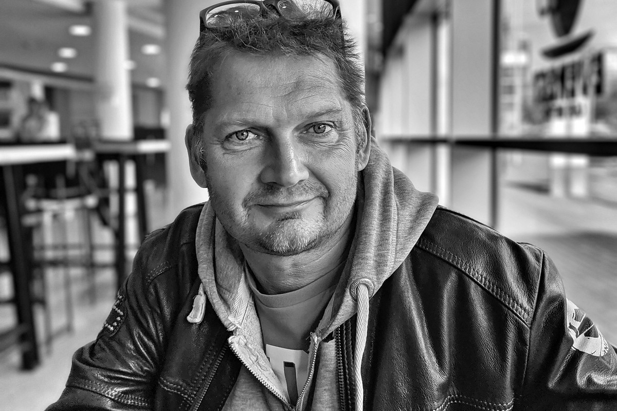 Sw-Portrait des Dozenten Jens Klocke, der in einem Café an einem Tisch sitzt in Lederjacke und Kapuzenpulli