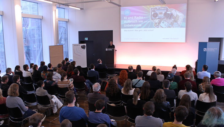 Blick auf den vollen Saal und die Bühne der Evangelischen Akademie. Dort steht Sandra Müller und hält ihre Keynote