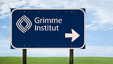 Ein Straßenschild vor einer grünen Wiese, das mit einem Pfeil nach rechts den Weg zum Grimme-Institut weist